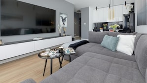 A modern living room with a large flat-screen TV, grey sofa, and a small coffee table. - Premium Apartment With Pool and Sauna (Dziwnów)
