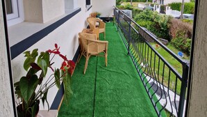 Een balkon met kunstgras, rieten meubilair en plantenpotten.