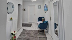 Een hal met een moderne plafondlamp, een spiegel, een deur en een blauwe stoel.