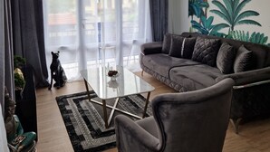 Een moderne woonkamer met een grijze bank, een glazen salontafel en een zwart-wit tapijt.