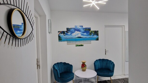 Een moderne kamer met twee blauwe stoelen, een ronde tafel, een grote spiegel en een plafondlamp.