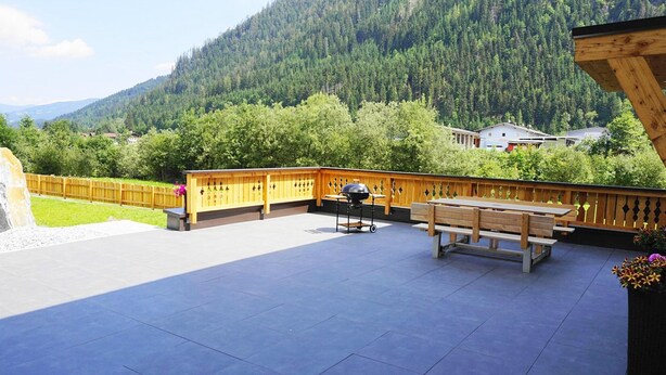 Eine Terrasse im Freien mit Holzdeck, Grill und Tisch.