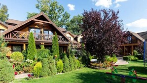 Ein Chalet mit Holzfassade, einem gepflegten Rasen und verschiedenen Bäumen und Sträuchern.