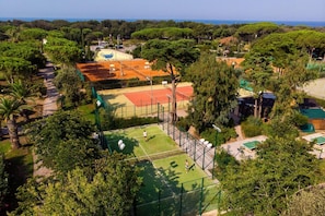Een tennisbaan omgeven door weelderig groen met een helder uitzicht op zee.