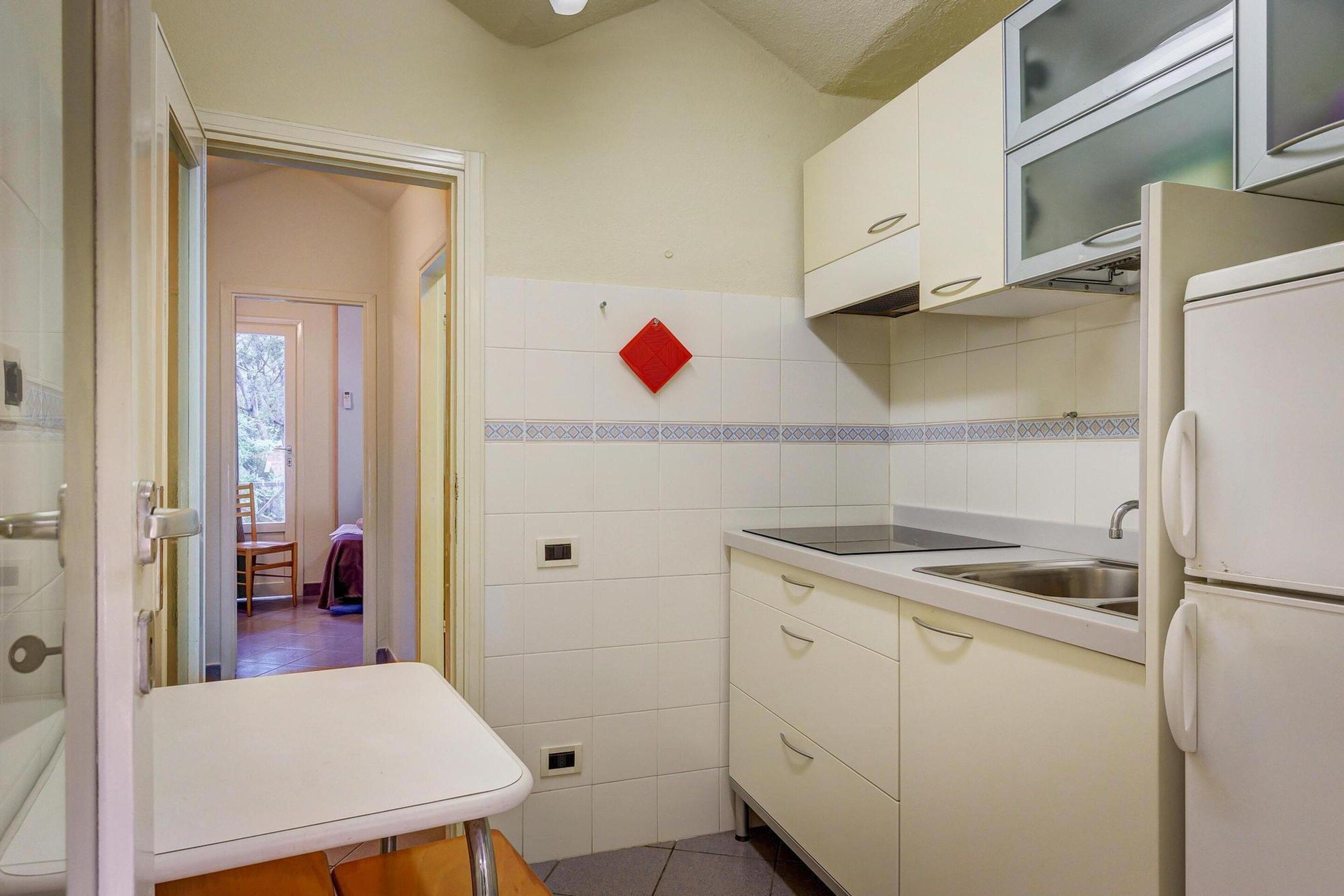 A compact kitchen with white cabinets, a built-in microwave, a sink, and a small dining table.