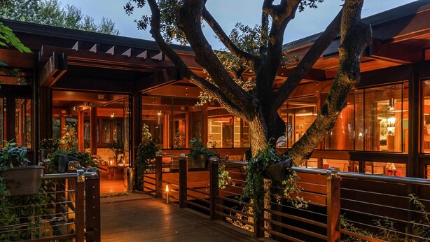 A wooden deck leading to a building with large windows and a tree in the center. - Resort Riva Degli Etruschi, San Vincenzo (San Vincenzo)