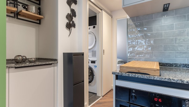 A compact kitchen with a built-in oven, a microwave, and a washing machine in the adjacent space. - Charmante Ferienwohnung (Büsum)