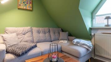 Een knus woongedeelte met een grijze bank, een houten salontafel en een schilderij aan de muur.