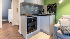 A compact kitchen with grey cabinets, a built-in oven, and a green accent wall. - Charmante Ferienwohnung (Büsum)