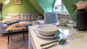 A modern dining area with a table set for two, a sofa, and a painting on the wall. - Charmante Ferienwohnung (Büsum)