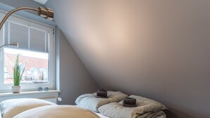 A bedroom with a bed, a window with blinds, a potted plant, and a bedside table with a lamp. - Charmante Ferienwohnung (Büsum)