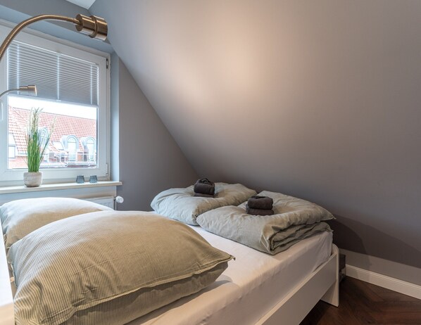 Une chambre à coucher avec un lit, une fenêtre avec des stores, une plante en pot et une table de chevet avec une lampe.