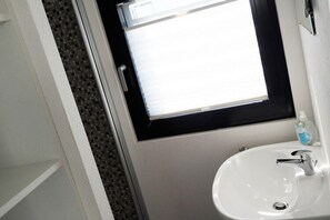 Un baño con un lavamanos blanco, una ventana con marco negro y una botella de jabón para manos sobre el lavamanos.