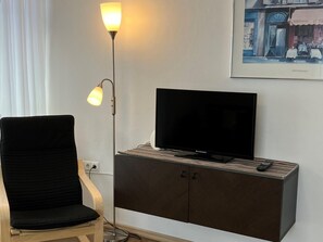 A room with a black chair, a television on a wooden cabinet, and a floor lamp. - Apartment in Axams Near Axamer Lizum (Axams)