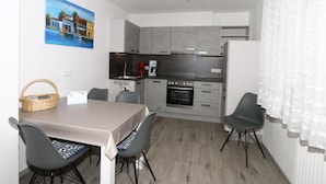 Una cocina moderna con armarios grises, horno empotrado y cafetera. Hay una mesa de comedor con sillas y una cesta en la encimera.