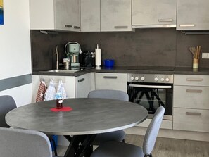 A modern kitchen with a round dining table, grey chairs, and stainless steel appliances. - Apartment in Axams Near Axamer Lizum (Axams)