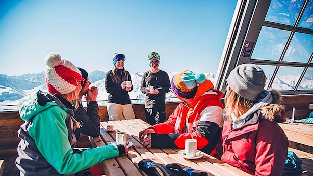 Un grupo de personas sentadas a una mesa de madera al aire libre, con vistas a la montaña.