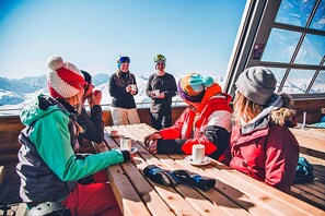 Un groupe de personnes est assis autour d’une table en bois, à l’extérieur, avec une vue sur la montagne.