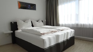 Una habitación de hotel moderna con una cama grande, una mesita de noche, un cuadro colgado en la pared y una ventana con cortinas traslúcidas.