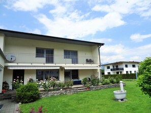 A two-story house with a balcony, a stone wall, and a well-maintained garden with flowers and a stone fountain. - Apartment in Axams Near Axamer Lizum (Axams)