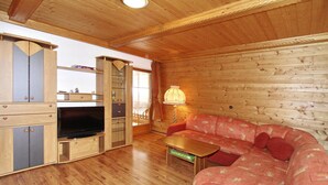 Een houten interieur met een bank, televisie, kastjes en een lamp.