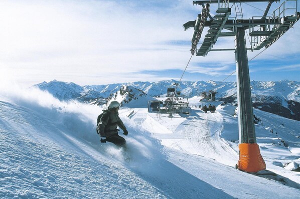 A snowboarder descending a snowy slope with a ski lift and mountains in the background. - House in Krimml Near Waterfalls & Hiking Trails (Krimml)