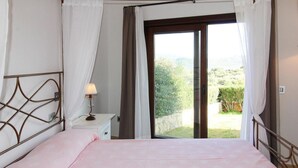 Een slaapkamer met een bed, een nachtkastje, een lamp en uitzicht op een tuin via een schuifdeur.