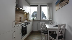 Une cuisine de taille réduite, avec des meubles blancs, une cuisinière et une fenêtre donnant sur un immeuble.