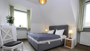 Une chambre à coucher avec un lit, des lampes de chevet, une chaise et une fenêtre avec des rideaux.