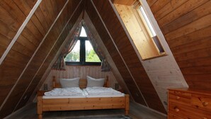 A bedroom with a sloped ceiling, a wooden bed, a dresser, and a window with curtains. - Ferienhaus mit Terrasse, Haustierfrei (Clausthal-Zellerfeld)