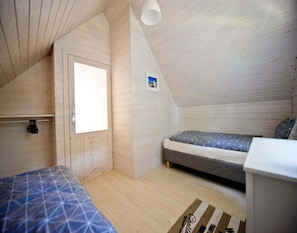 A small, sloped-roofed room with two beds, a wooden door, and a small window. - Holiday Home Pobierowo Near Baltic Beach (Rewal)