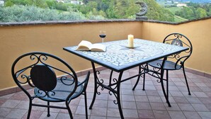 Una terraza con una mesa, dos sillas, un libro abierto, una copa de vino tinto y una vela.