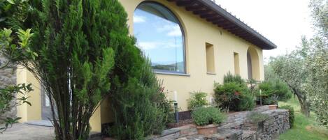 Un edificio giallo con un muro di sostegno in pietra, un'ampia finestra e diverse piante.