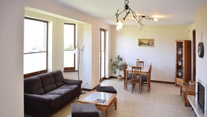 Una sala de estar con un sofá, una mesa de centro y un juego de comedor. Hay una chimenea, una estantería y una planta en maceta.