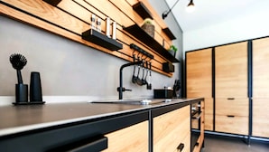 A modern kitchen with wooden cabinets, a black countertop, and a hanging pot rack. - Exklusives Landhaus auf Fehmarn (Fehmarn)