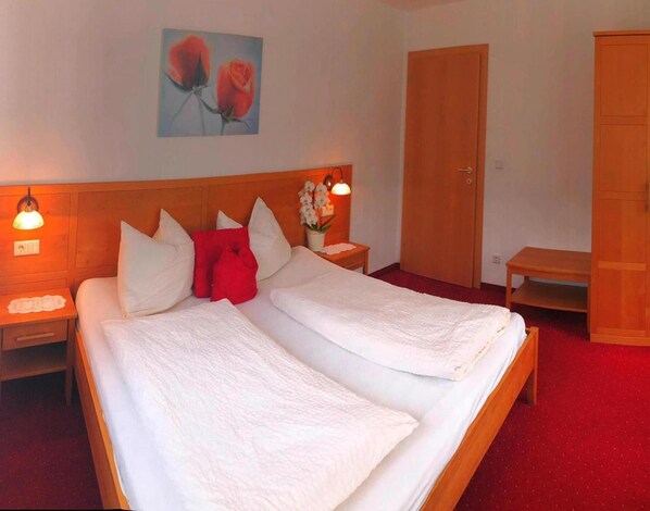 A hotel room with two beds, a wooden headboard, a red carpet, a wooden wardrobe, and a painting of roses on the wall. - Apartment in Goldrain With Pool & Mountain Views (Laces)