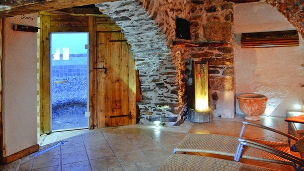 A rustic interior with a wooden door labeled "Doccia," a stone wall, a tiled floor, and a wicker chair. - Apartment in Pellizzano With Paid Sauna (Pellizzano)
