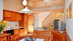 A kitchen with wooden cabinets, a dining table with chairs, a television, and a staircase. - Apartment in Pellizzano With Paid Sauna (Pellizzano)