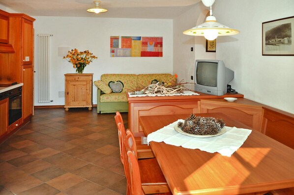 A cozy living room with a wooden dining table, a sofa, a television, and a cabinet. - Apartment in Pellizzano With Paid Sauna (Pellizzano)
