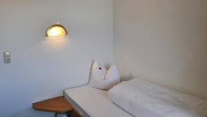 A small, single-bed room with a curved wall-mounted light fixture and a wooden nightstand. - Apartment Val Sinestra, Kappl (Kappl)