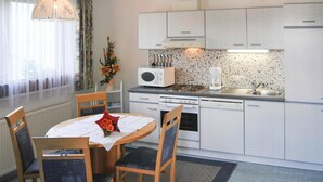 A compact kitchen with white cabinets, a built-in oven, a microwave, and a sink. There is a dining table with chairs and a vase of flowers. - Apartment Val Sinestra, Kappl (Kappl)
