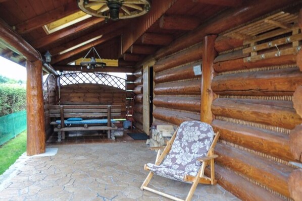 A log cabin with a stone patio, a wooden bench, and a lounge chair. - Holiday Home in Kopalino (Choczewo)