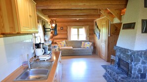 Een gezellig interieur van een chalet met een keuken, eethoek en een stenen open haard.