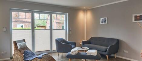 Un salon moderne avec un fauteuil en osier aux lignes courbes, un canapé gris et une petite table basse.