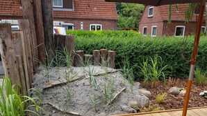 A garden with a wooden deck, a small pond with plants, and a brick house in the background. - Das Ferienhus in Tonning (Toenning)