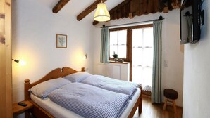 Un dormitorio con cama de madera, lámpara colgante, ventana con cortinas y un radiador.