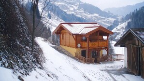 Una cabaña de madera con techo inclinado, un balcón y vistas de montañas nevadas.