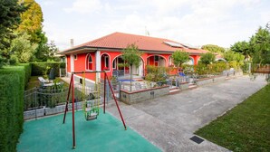A red house with a green playground in front, surrounded by trees and a clear sky. - Apartment in Cilento Near Sandy Beach (Ascea)