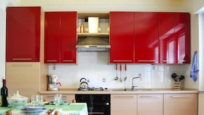 A compact kitchen with red cabinets, a coffee machine, a kettle, and a dishwasher. - Apartment in Cilento Near Sandy Beach (Ascea)