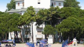 Um hotel à beira-mar com vários andares, área de estar ao ar livre com guarda-sóis e um parquinho infantil.